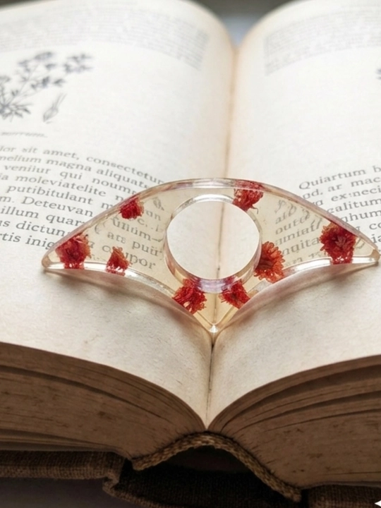 Bir qoʻlda oʻqish uchun kitob sahifalarini ushlab turuvchi tutqich, quruq gullar bilan - 